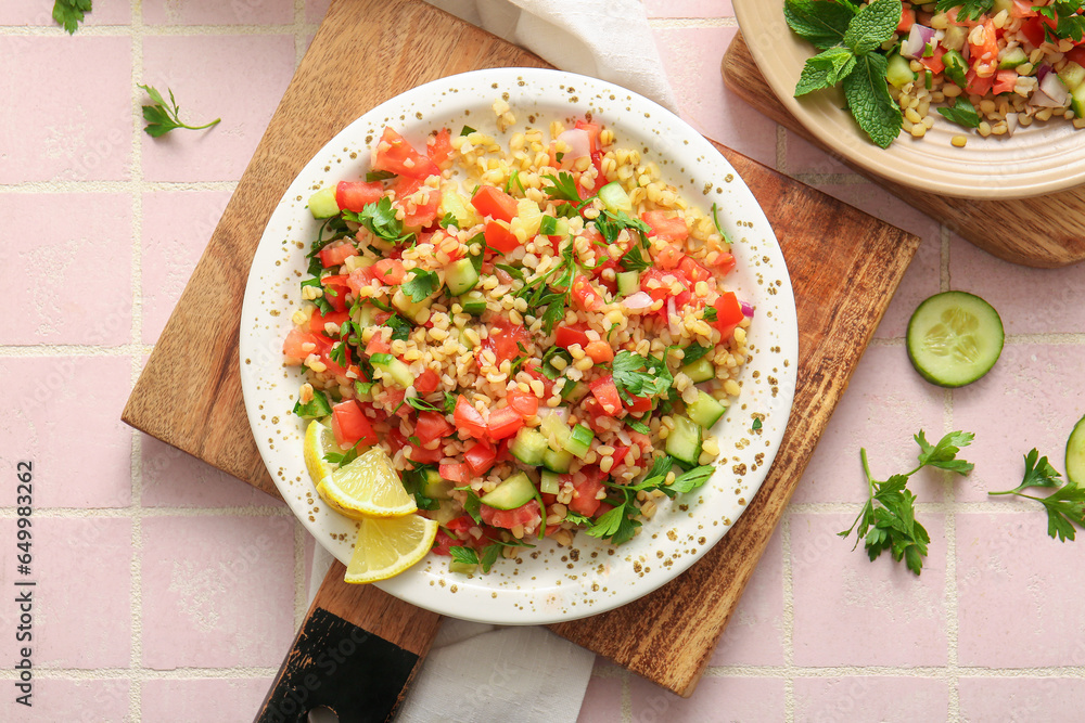 Plate with delicious tabbouleh salad on pink tile background