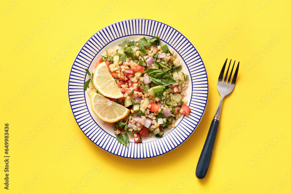 Plate with delicious tabbouleh salad and lemon slices on yellow background