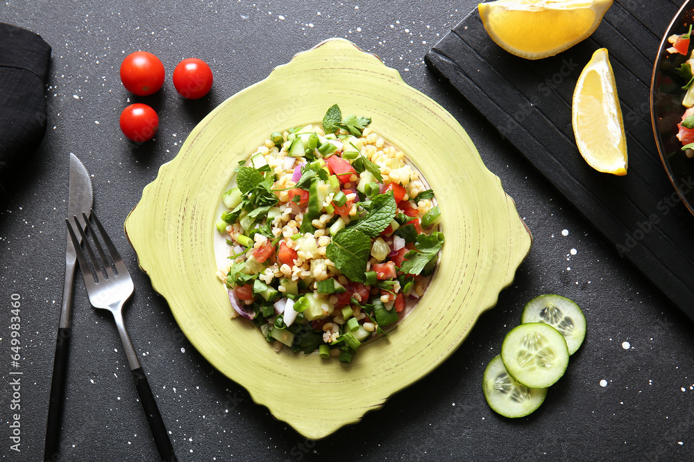 Plate with delicious tabbouleh salad and cutlery on dark background