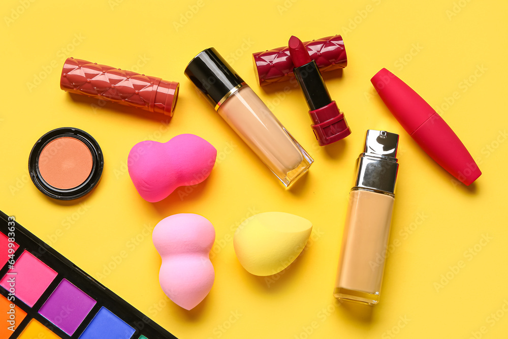 Composition with decorative cosmetics and makeup sponges on yellow background