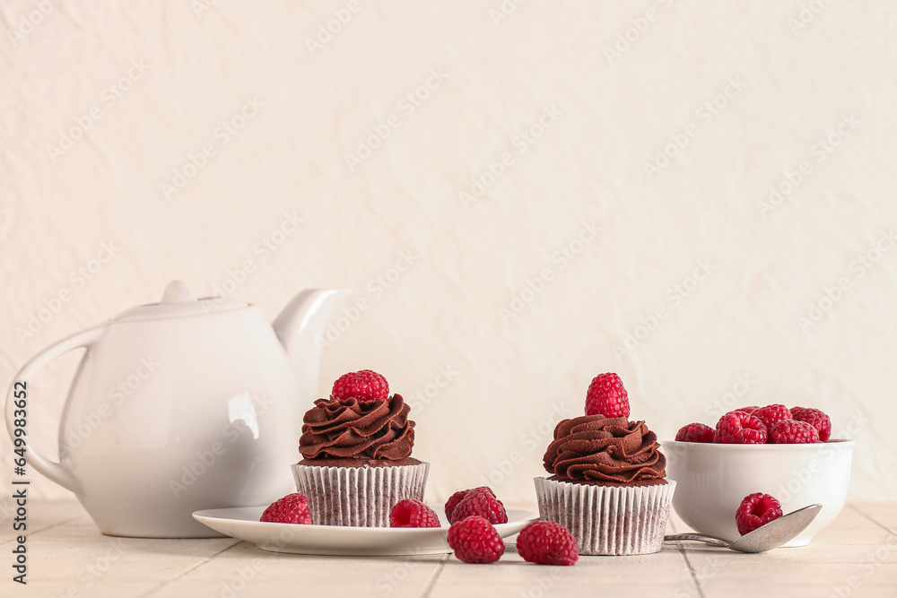 Tasty chocolate cupcakes with raspberries and teapot on table