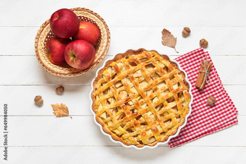 Baking dish with delicious apple pie and cinnamon on white wooden background