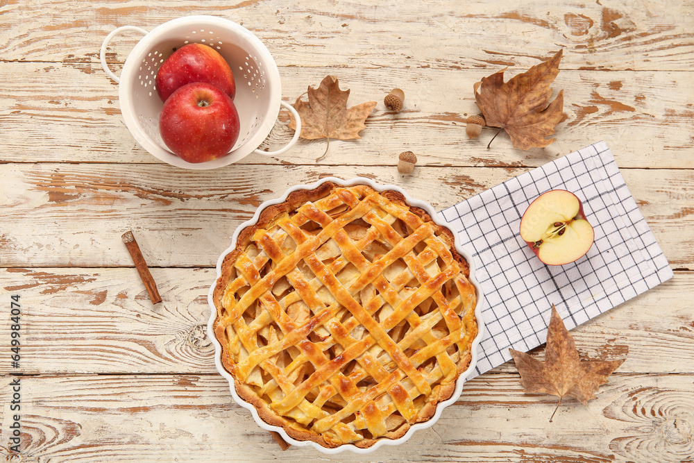 Baking dish with delicious apple pie and ingredients on white wooden background