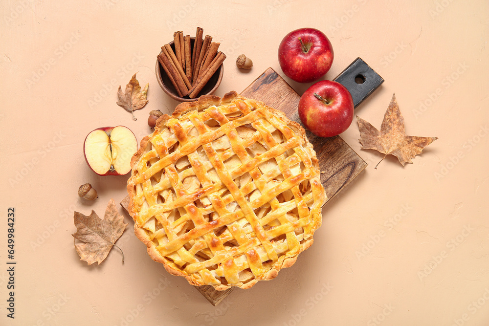 Wooden board with delicious apple pie and ingredients on orange background