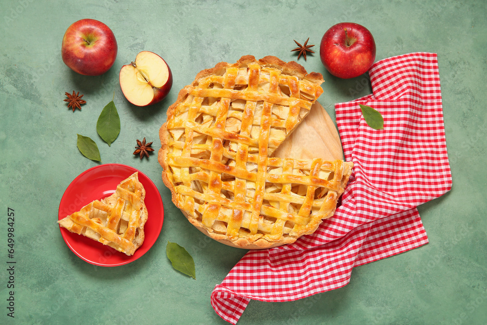 Wooden board with delicious apple pie on green background