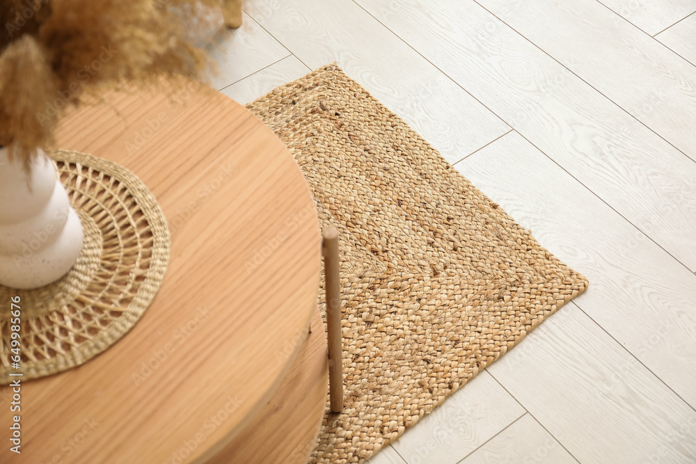 Stylish wicker rug and coffee table with vase in living room