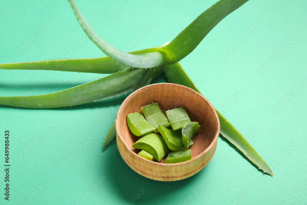 Aloe vera plant with slices in wooden bowl on green background, closeup