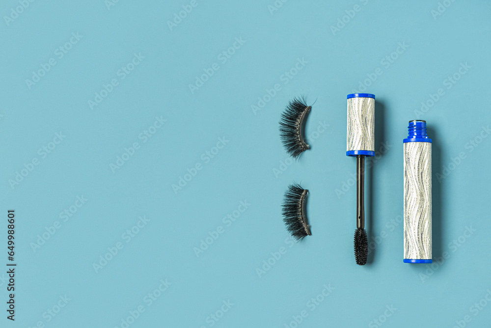 Black mascara in silver tube and fake eyelashes on blue background