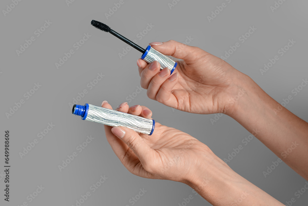 Woman holding black mascara in silver tube on beige background