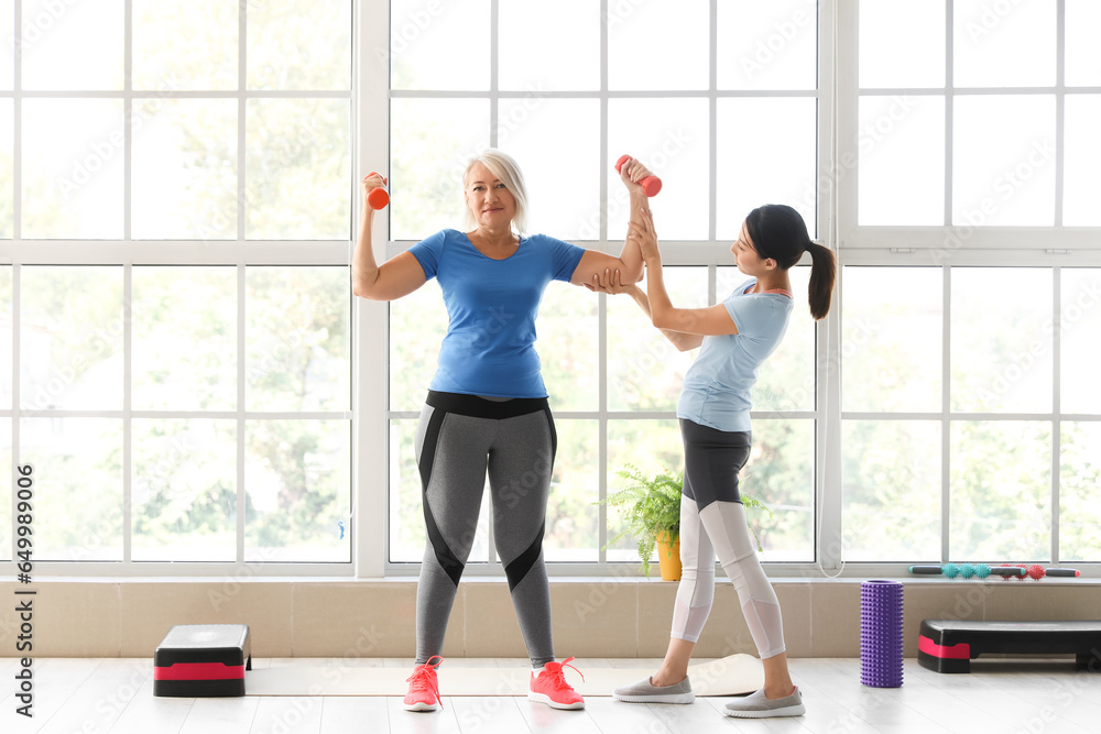 Mature woman training with dumbbells and therapist in rehabilitation center