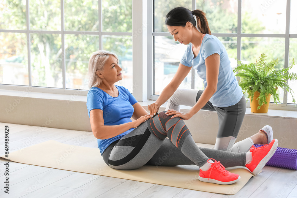 Mature woman training with therapist on mat in rehabilitation center