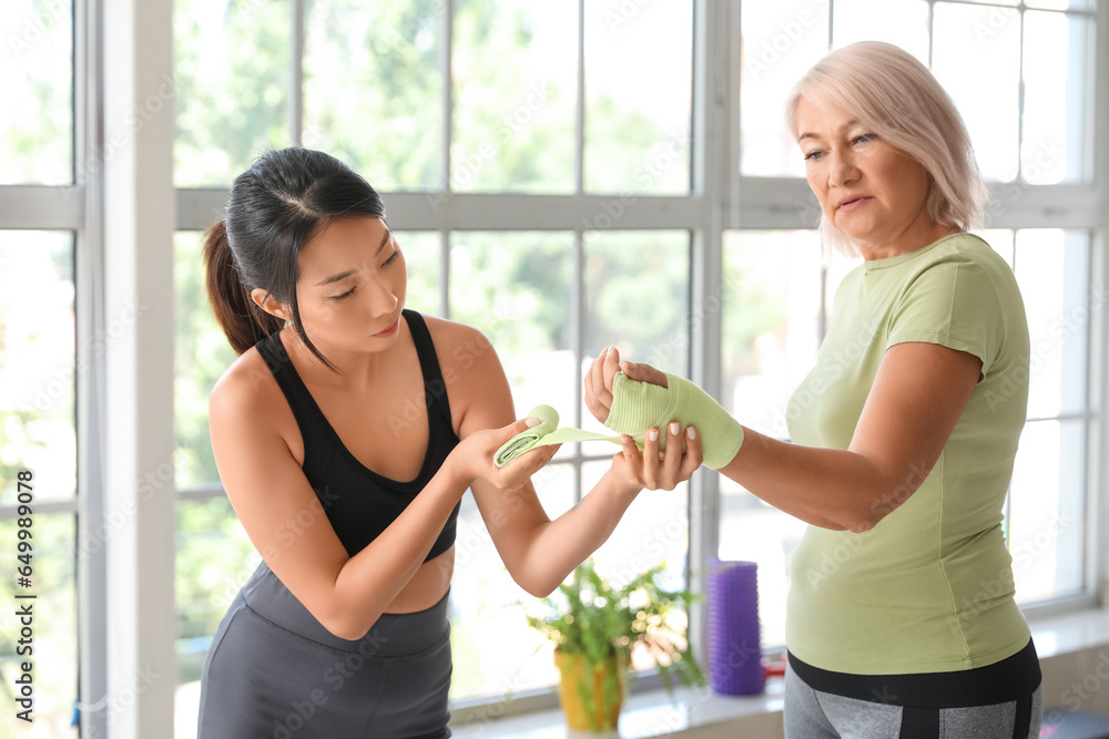 Mature woman with therapist applying wrist wrap in rehabilitation center