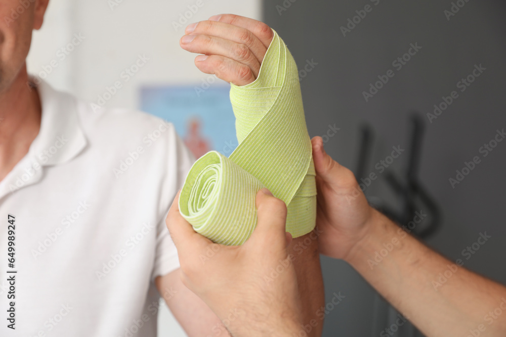 Mature man with therapist wrapping wrist in rehabilitation center, closeup