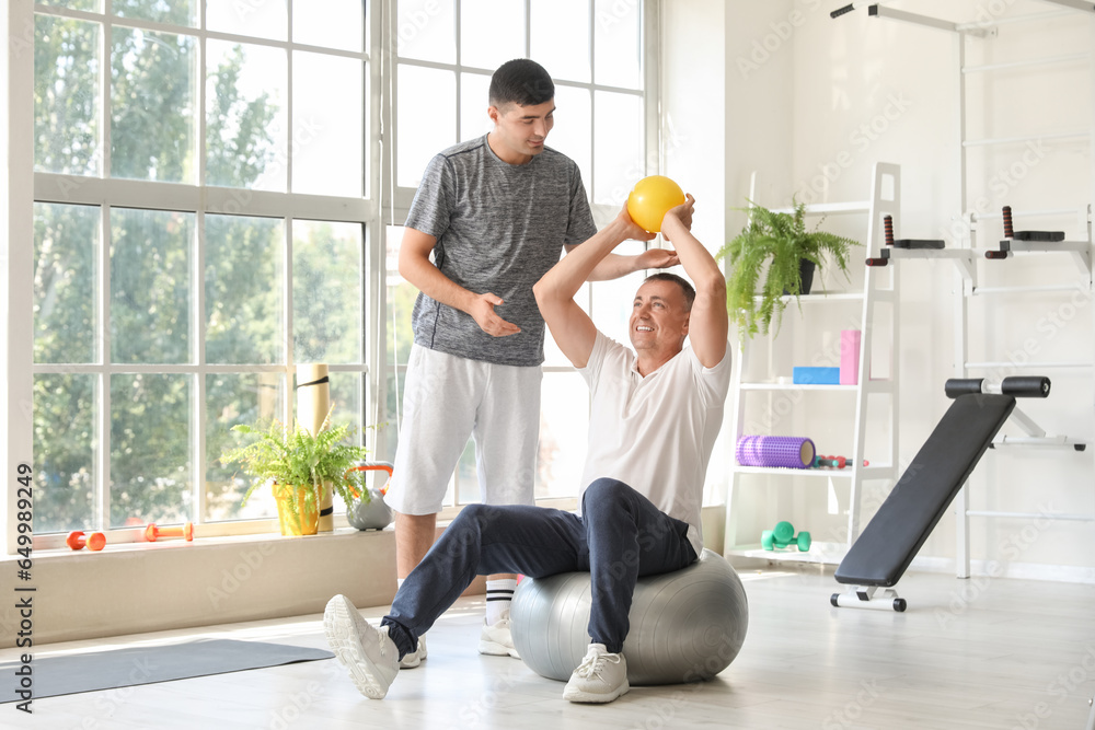 Mature man training on fitball with therapist in rehabilitation center