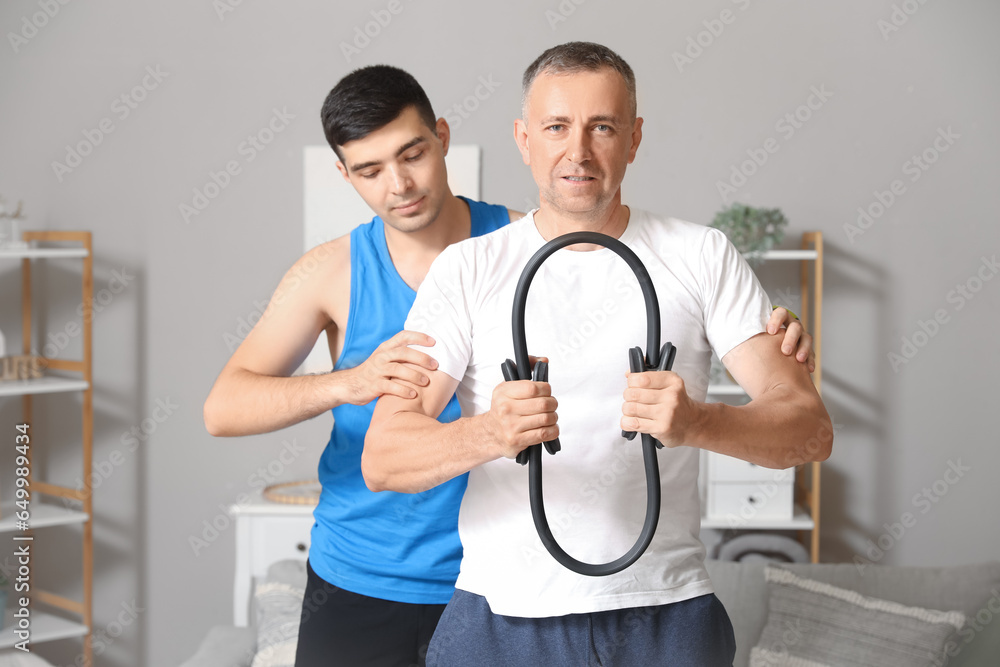 Mature man training with pilates circle and rehabilitation therapist at home