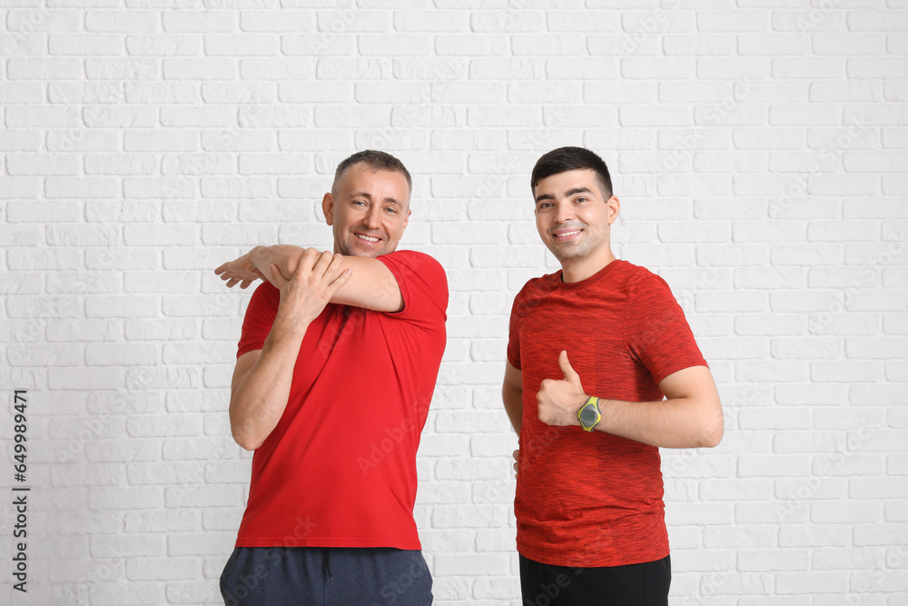 Mature man with rehabilitation therapist on white brick background