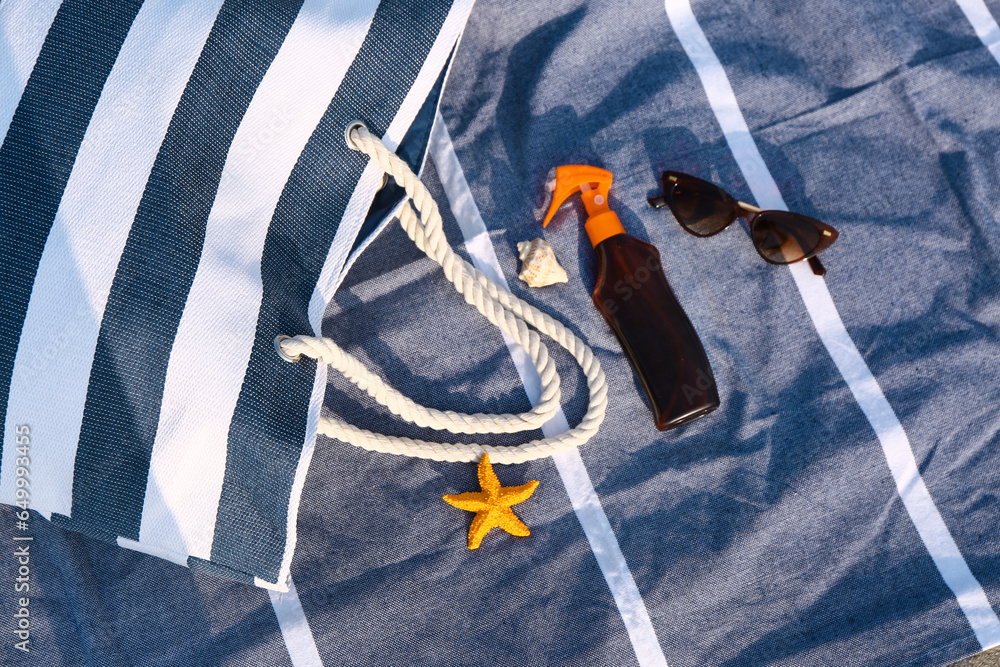 Beach bag, bottle of sunscreen and sunglasses on towel outdoors, closeup