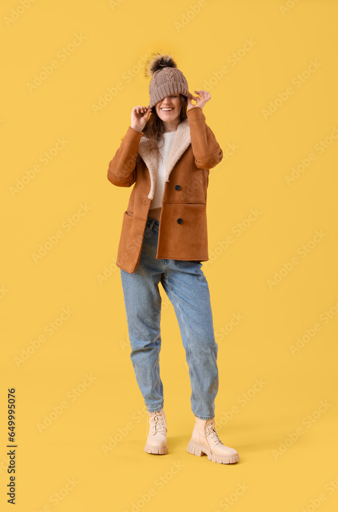 Young woman in winter clothes on yellow background