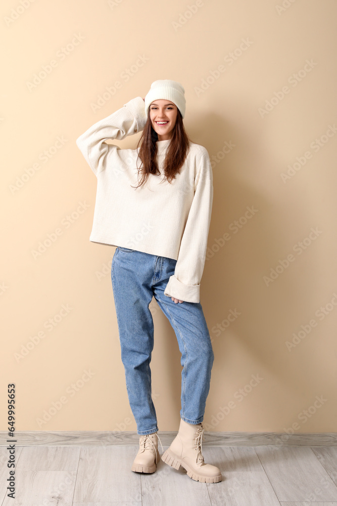 Young woman in winter clothes near beige wall