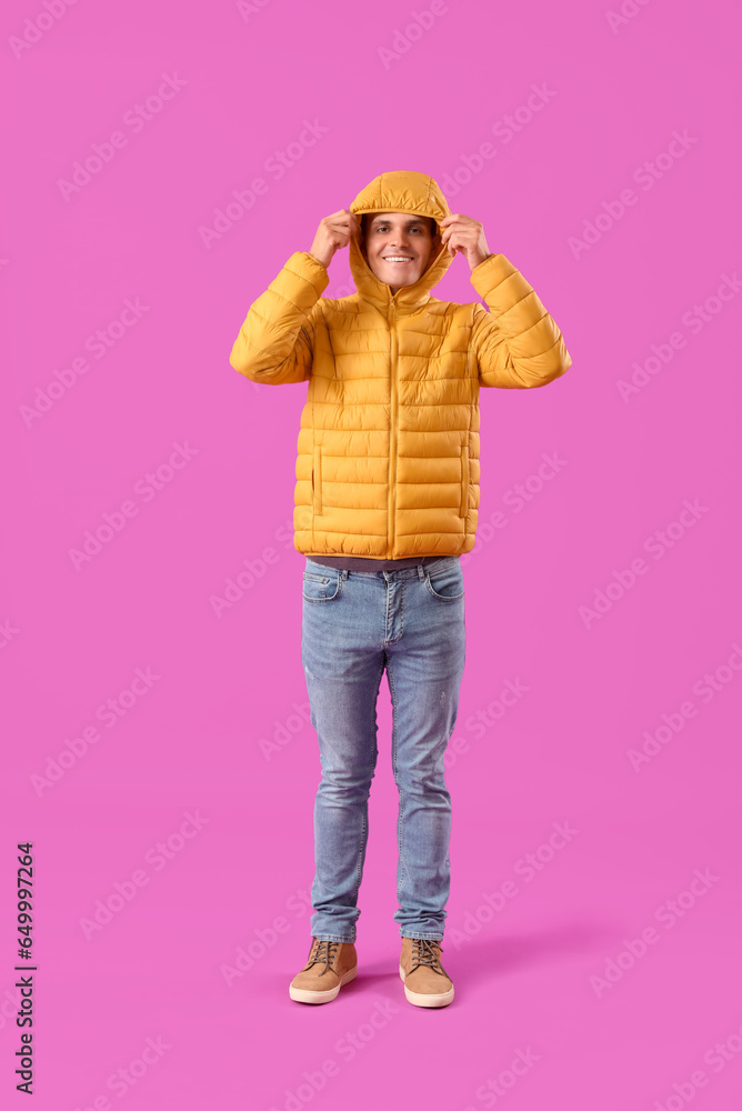 Young man in warm puffer jacket on purple background