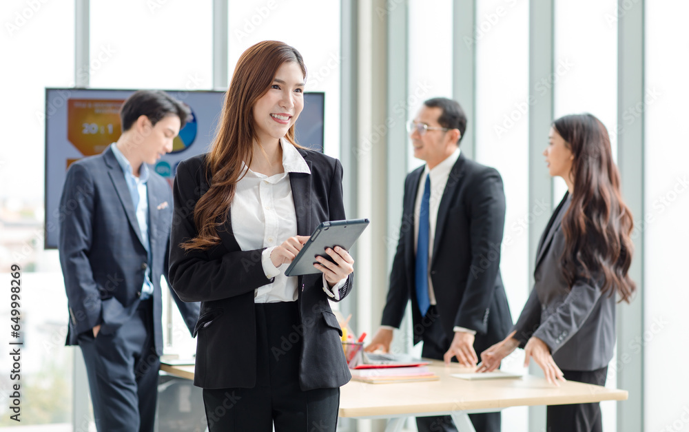 Portrait shot of Asian professional successful female businesswoman manager entrepreneur in formal suit standing smiling looking at camera holding touchscreen tablet computer in company meeting room