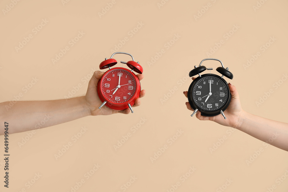 Hands holding different alarm clocks on beige background