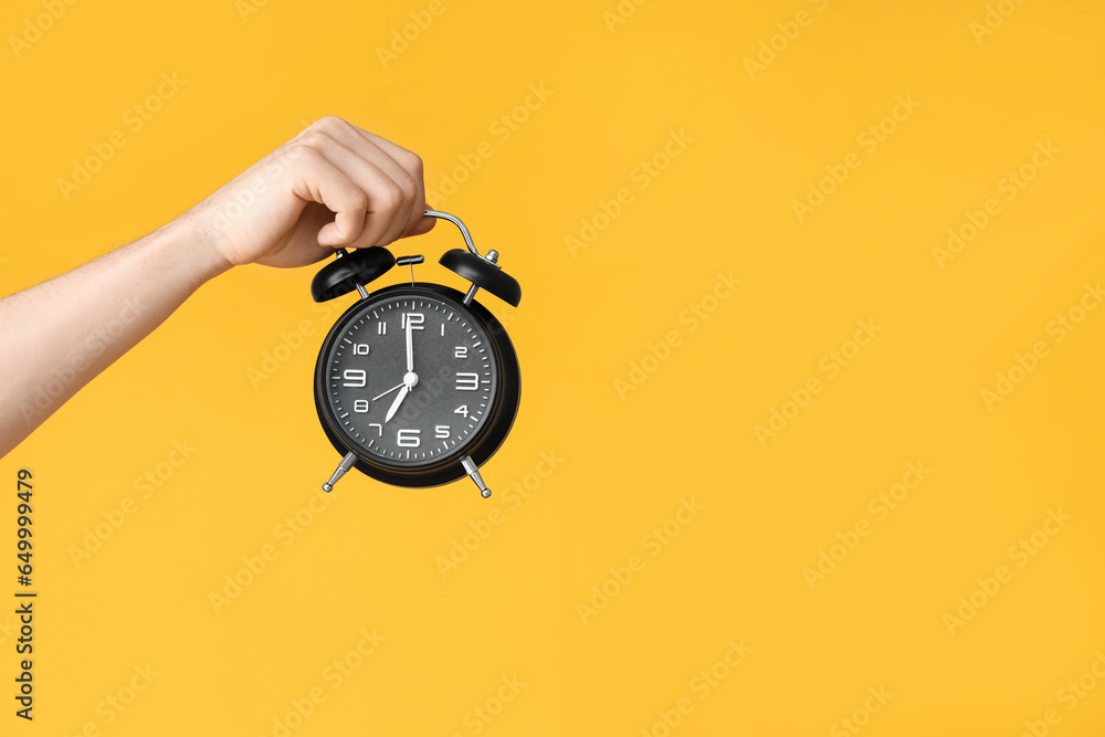 Male hand holding alarm clock on yellow background