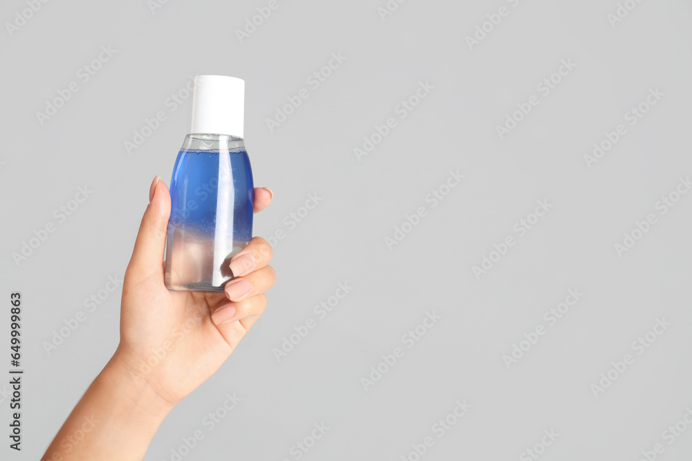 Young woman with bottle of micellar water on light background, closeup