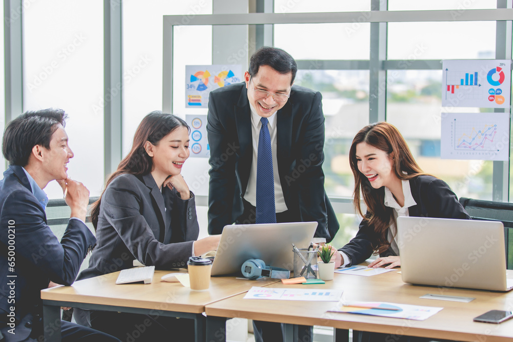 Asian professional successful businessman manager entrepreneur in formal suit standing teaching brainstorming marketing strategy with male female businesswomen employees team in company meeting room