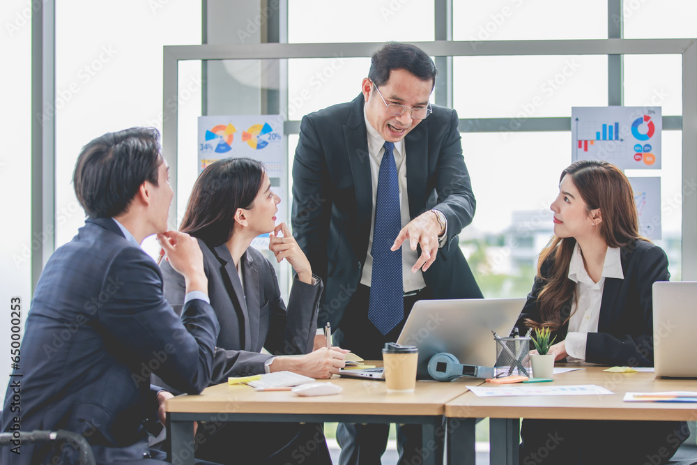 Asian professional successful businessman manager entrepreneur in formal suit standing teaching brainstorming marketing strategy with male female businesswomen employees team in company meeting room