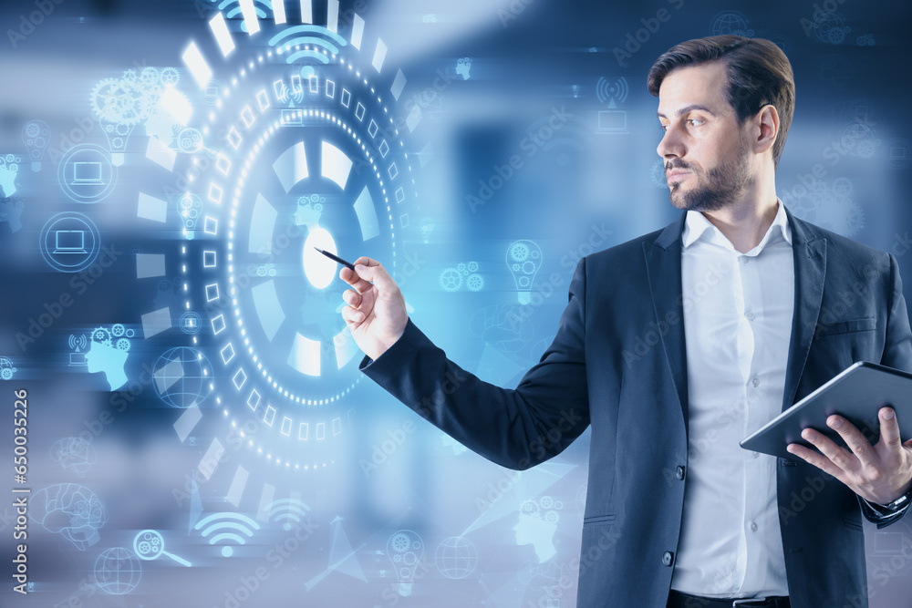 Attractive european businessman with pen using glowing digital business interface with cogwheels and other icons on blurry office interior background. Future, innovation and technology concept.