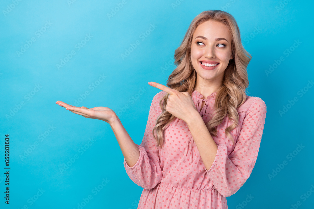 Photo of pretty woman with wavy hairdo dressed pink clothes look indicating at sale on arm empty space isolated on blue color background