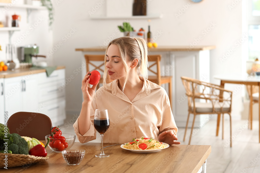 Young woman with fresh tomato eating pasta in kitchen