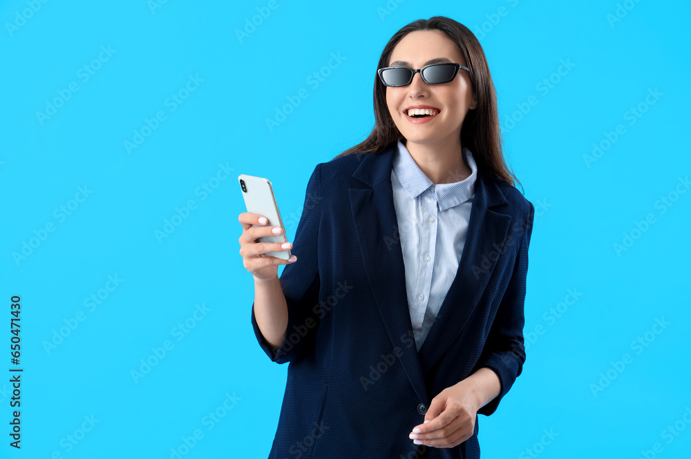 Young woman in stylish suit with mobile phone on blue background