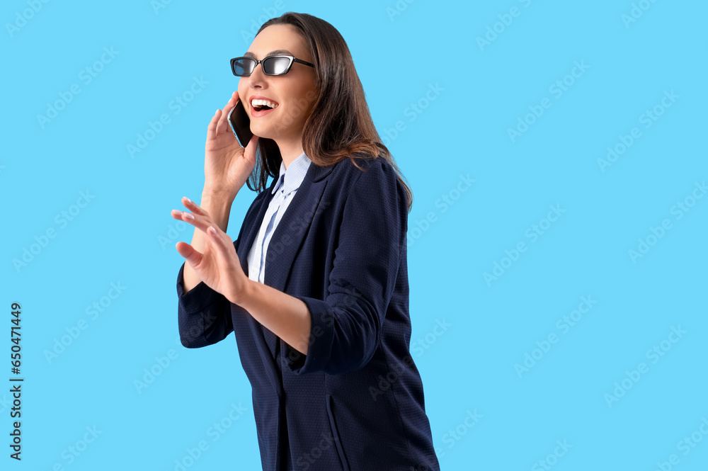 Young woman in stylish suit talking by mobile phone on blue background