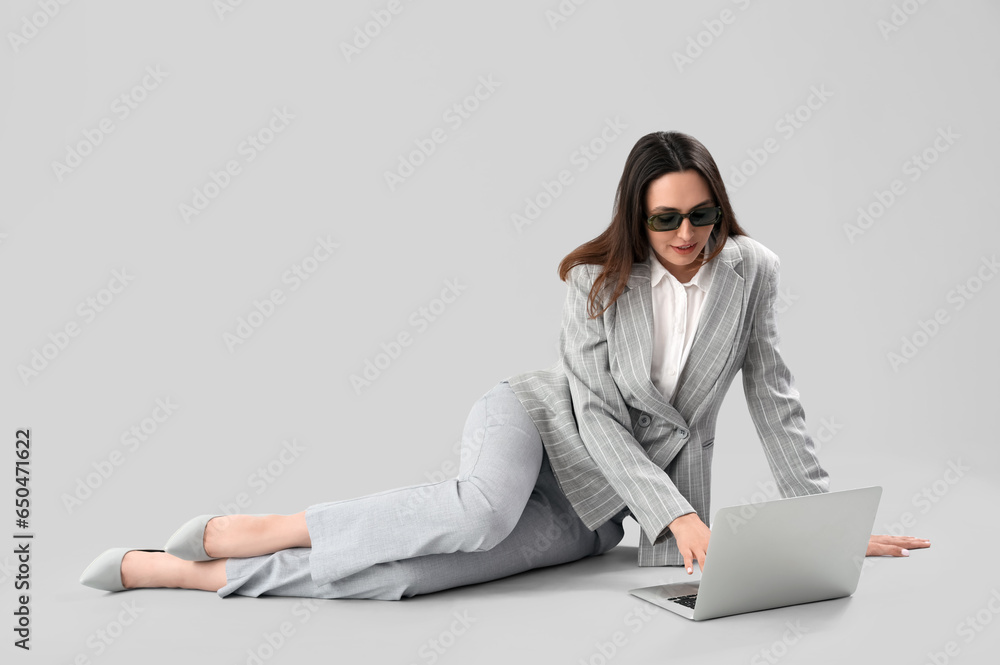 Young businesswoman in stylish suit using laptop on light background