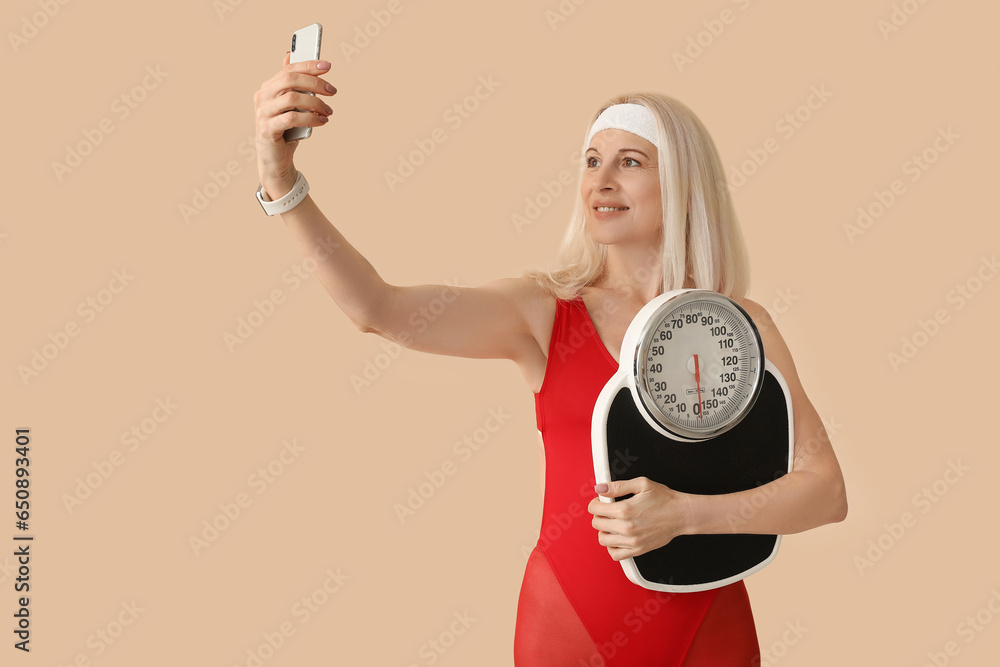 Sporty mature woman with scales and mobile phone taking selfie on beige background