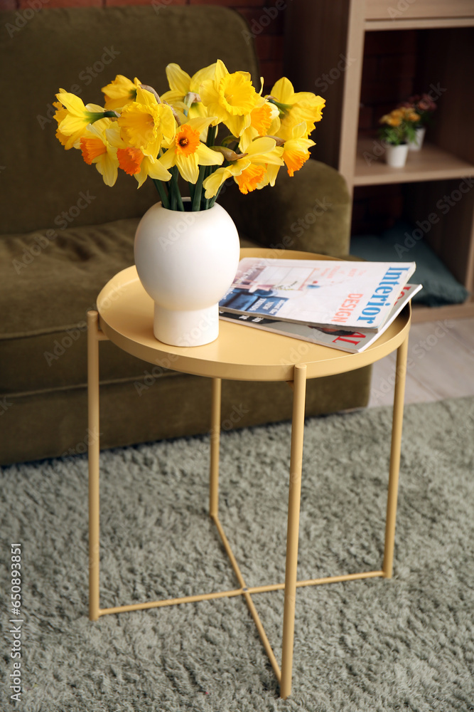 Vase with beautiful narcissus flowers and magazines on coffee table in living room