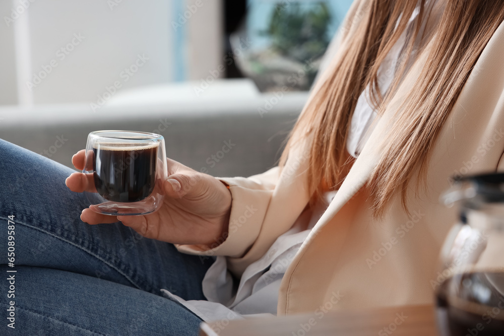 Woman sitting on sofa with glass of delicious coffee