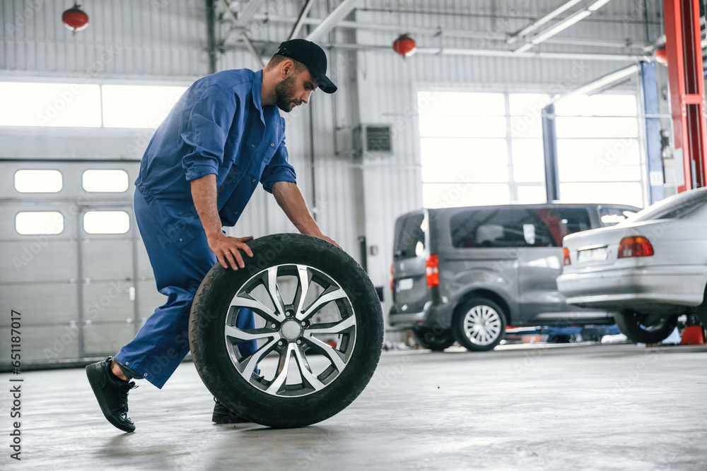 With brand new wheel. Auto mechanic working in garage. Repair service