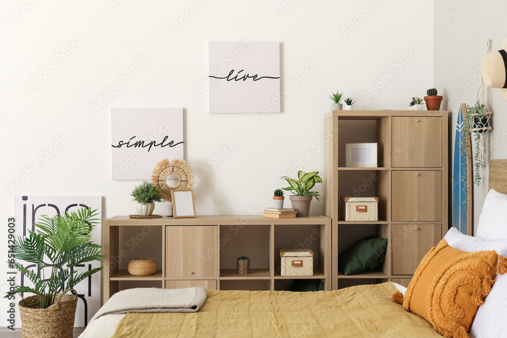 Interior of light bedroom with houseplants and shelving unit