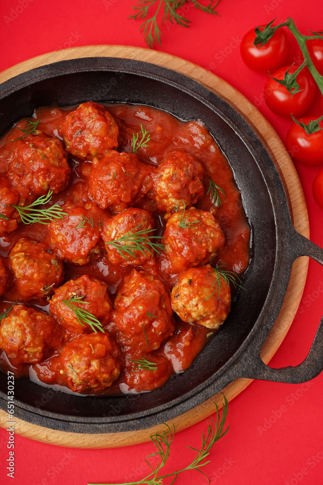 Frying pan of tasty meat balls with tomato sauce and dill on red background