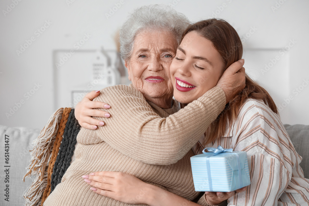 Senior woman greeting her granddaughter with gift at home