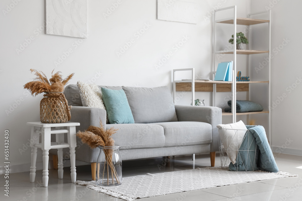 Cozy grey sofa and basket with soft blanket in interior of living room