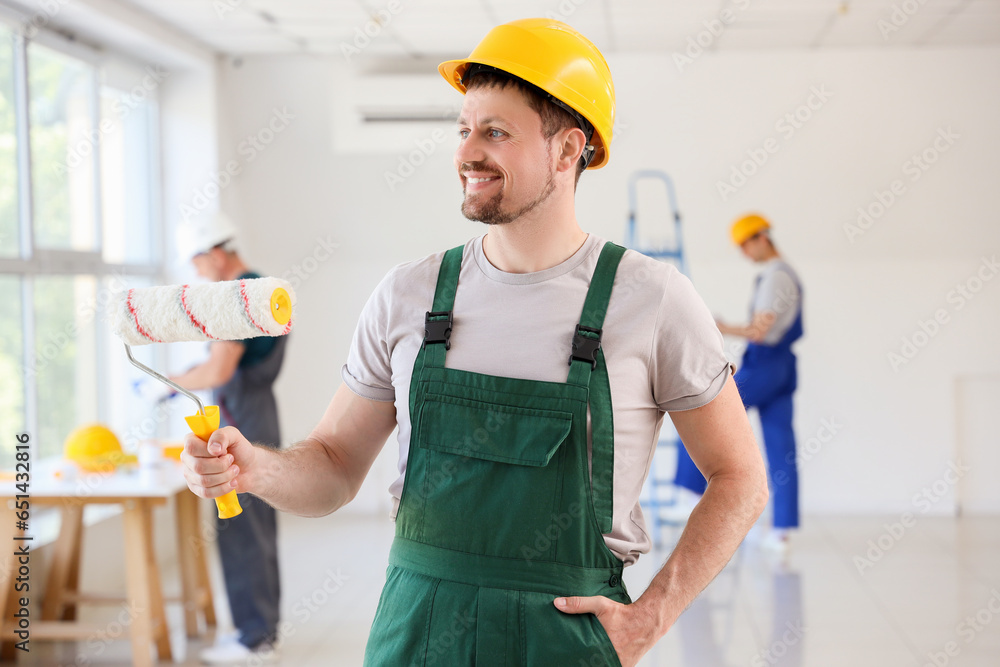 Male builder with paint roller in room