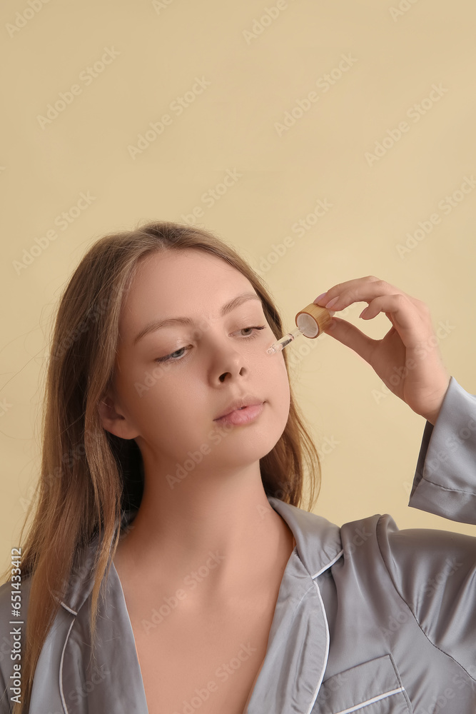 Pretty young woman with cosmetic oil on beige background