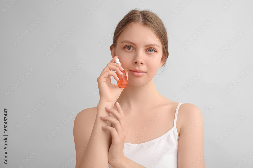 Pretty young woman with cosmetic oil on light background