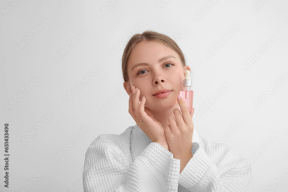 Pretty young woman with cosmetic oil on light background