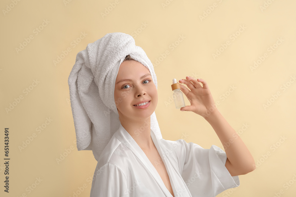 Pretty young woman with cosmetic oil on beige background