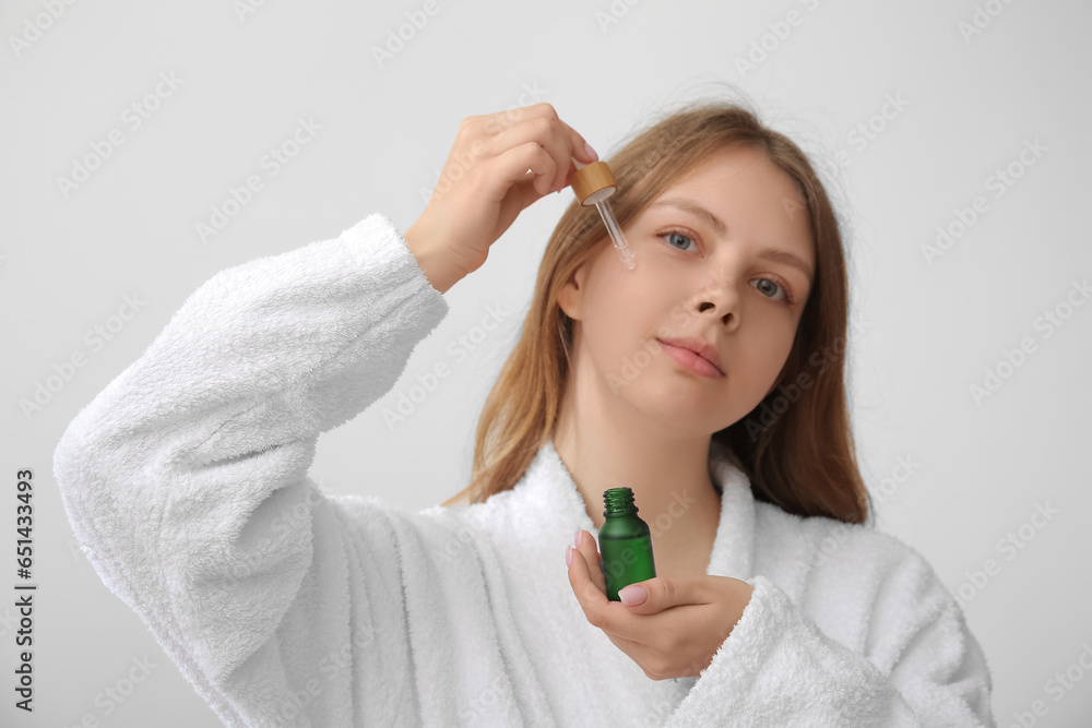 Pretty young woman with cosmetic oil on light background